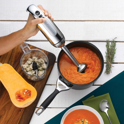 Heavy Hitting Immersion Blender Set With A Versatile Chop Bowl Whisk And Non Drip Measuring Jug Powered By 700W Turbo Motor In Polished Chrome Finish blending soup in a pot.
