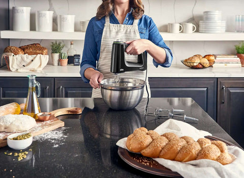 Woman using High Octane 350 Watt Hand Mixer With SmartMix Technology over a mixing bowl in a modern kitchen.