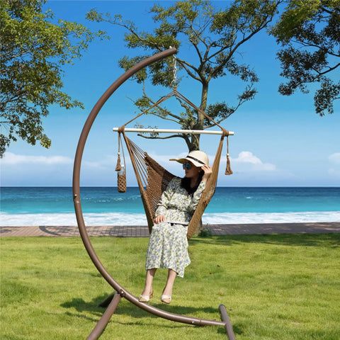 Person relaxing in Caribbean Style Rope Hammock Chair With 40 Inch Steel Spreader Bar And Anti Slip Rings, outdoor setting