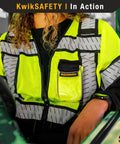 Women Class 3 High Visibility Safety Vest Featuring Cinched Elastic Waist Four Roomy Utility Pockets Snug Contour Tailored Hustle Ready Workday Essential in yellow mesh at a worksite.