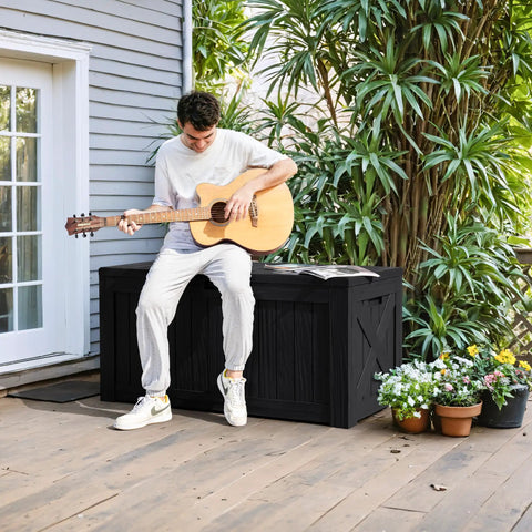 Man playing guitar sitting on 120 Gallon Outdoor Deck Box Heavy Duty Resin Construction Weatherproof Lockable Storage