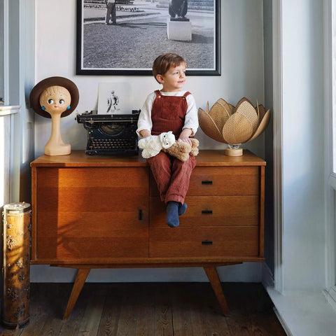 Child sitting on wooden cabinet with vintage typewriter and decorative items.