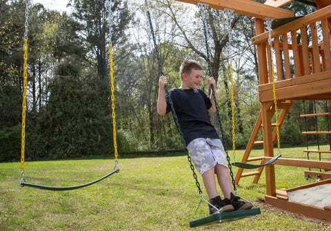 Child standing on green stand up swing for backyard playsets with 14x14 inch base, coated chains, attached to wooden playset