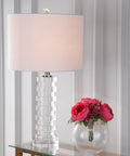 Clear Crystal Staggered Geometric Column LED Table Lamp With White Linen Drum Shade In Chrome Finish on a glass table with pink flowers.