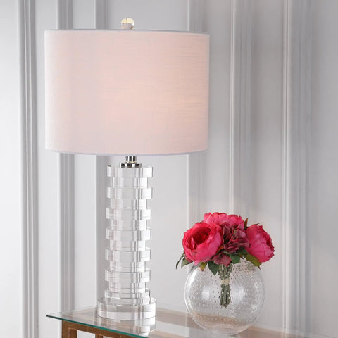 Clear Crystal Staggered Geometric Column LED Table Lamp With White Linen Drum Shade In Chrome Finish on a glass table with pink flowers.