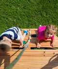Kids climbing double rock wall on Cedar Wood Swing Set with Wave Slide and Elevated Play Deck, backyard adventure fun