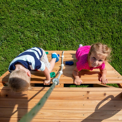 Kids climbing double rock wall on Cedar Wood Swing Set with Wave Slide and Elevated Play Deck, backyard adventure fun