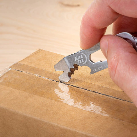 Hand using DoohicKey Keychain Multi Tool Stainless Steel 8 In 1 with serrated edge to open a cardboard box