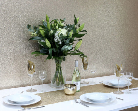 Gold Sequin Wallpaper Roll With Sparkle Finish accenting a dining area with white tableware and floral centerpiece.