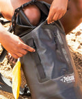 Person adjusting ExoDry 20L Drybag With Roll Top Compression Waterproof And Lightweight Gear Carrier With Shoulder Straps on sandy beach
