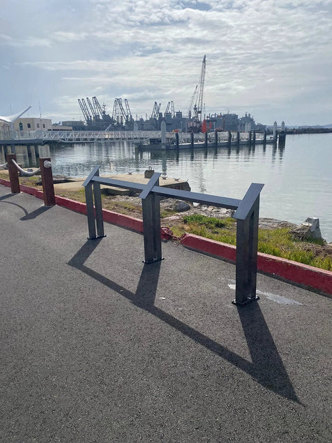 View of waterfront with metal structures on paved surface near water with cranes in the background