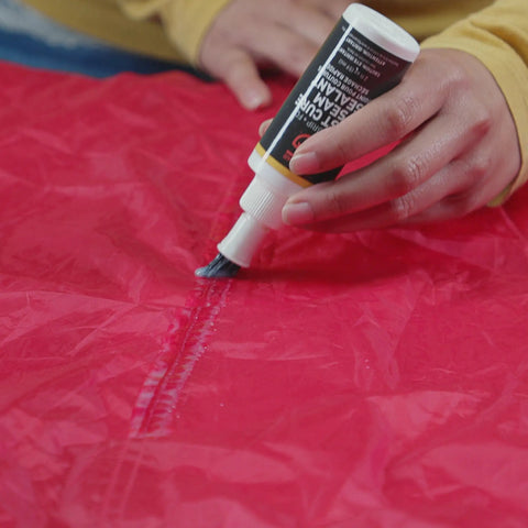 Applying Seam Grip FC Fast Cure Sealant For Tents Rainflies Tarps And Awnings Water Based Seam Sealer on red nylon fabric