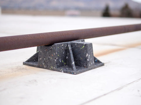 Saddle Support Rooftop Pipe Stand in speckled recycled plastic; metal pipe resting on cradle.