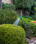 Gardener using 36 Inch Front Trigger Watering Wand Hose Nozzle With Carbon Fiber Texture And Non Slip Grip on bush