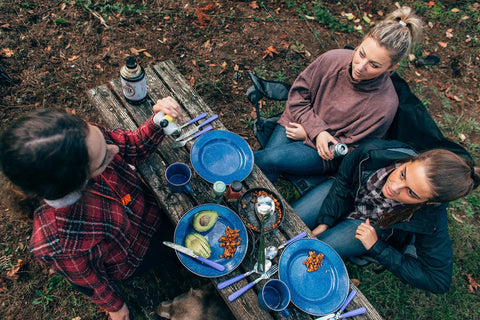 Three people dining outdoors with Deluxe 24 Piece Enamel Tableware Set With Blue Finish For Four People Durable Steel Dinnerware