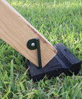 Wooden swing set post secured by large molded rubber block on grass, part of Leveling Kit For Swing Sets with Six Large Molded Rubber Blocks.
