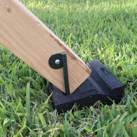 Wooden swing set post secured by large molded rubber block on grass, part of Leveling Kit For Swing Sets with Six Large Molded Rubber Blocks.