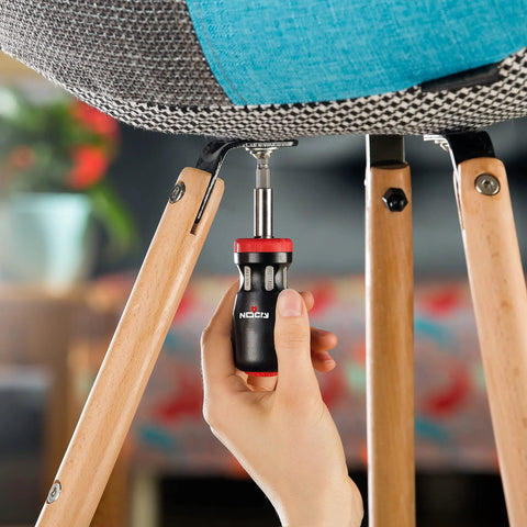 Person using Stubby Ratcheting Screwdriver Kit With 14-In-1 Mini Bit Set Including Flathead, Hex, Torx, Square, And Pozidriv Tips Compact Black And Red Dope Handy Tool For Quick Fixes And Electronics Projects to tighten chair screw indoors.
