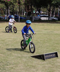 Kids biking over a sturdy ramp in a park, highlighting Sturdy Jump Ramp For Skateboard, Bike, Scooter, BMX, RC Car And Dirt Bike 25.2 Inch
