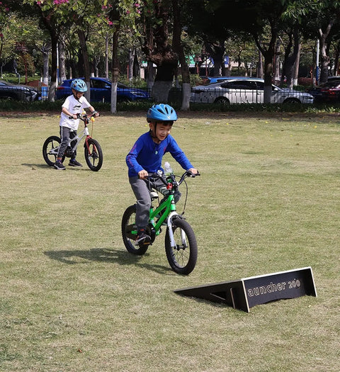 Kids biking over a sturdy ramp in a park, highlighting Sturdy Jump Ramp For Skateboard, Bike, Scooter, BMX, RC Car And Dirt Bike 25.2 Inch