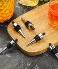 Eight stainless steel wine bottle stoppers with black rubber O-rings on a wooden board.