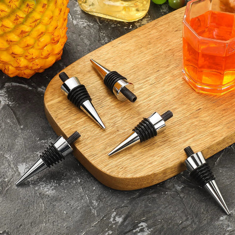 Eight stainless steel wine bottle stoppers with black rubber O-rings on a wooden board.