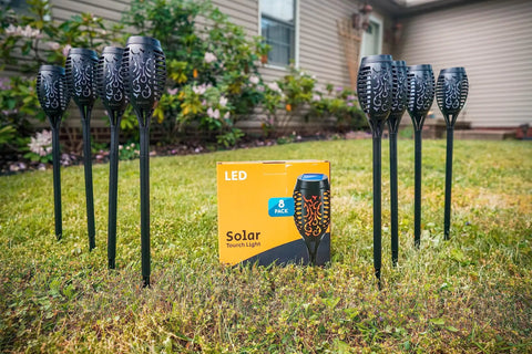 Outdoor Solar Flickering Torch Lights 8 Pack Waterproof Patio Tiki Lamps With 12 LED Flame Beams arranged in a garden