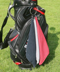 Black, grey, and red Microfiber Golf Towel 16 By 16 Inches With Carabiner Clip hanging on golf bag on grass