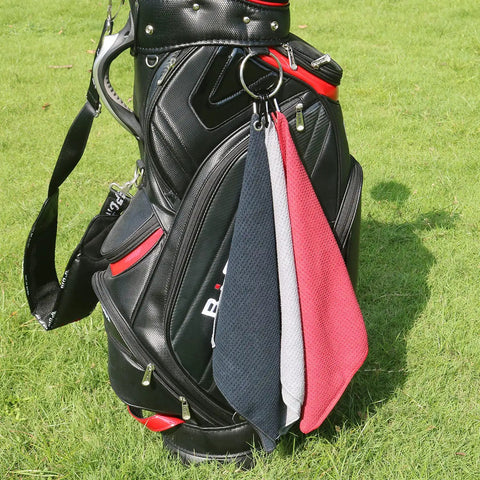 Black, grey, and red Microfiber Golf Towel 16 By 16 Inches With Carabiner Clip hanging on golf bag on grass