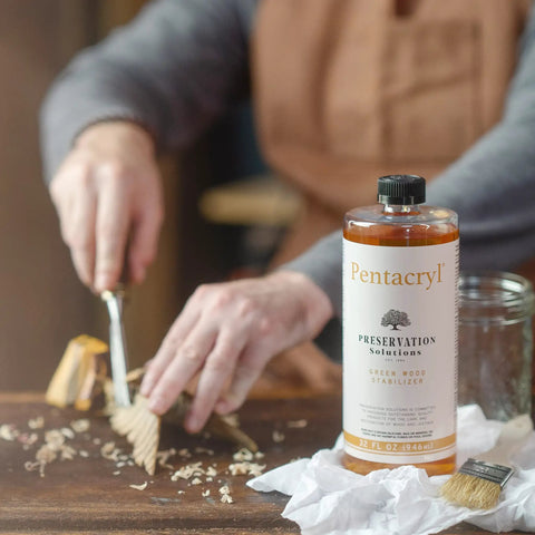 Person carving wood with a tool beside a bottle of Pentacryl Green Wood Stabilizer For Fresh Cut Wood That Keeps It From Cracking And Shrinking Deep Penetration For Woodturning And Carving Projects Perfect For Pro Woodworkers And DIY Furniture Makers on a table.