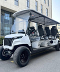 White Eight Passenger Electric Golf Cart Rolled Up Tight With Beefy Dual Arm Suspensions Silky Smooth Five Kilowatt Motor Plus Touchscreen Audio And Deep Reclining Lounge Seats parked in front of a building.