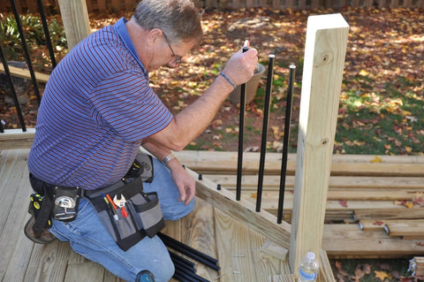 Person installing 10 Pack Three Quarters Inch Round 36 Inch Length Black Powder Coat Balusters For Staircase Deck Porch Rails With Easy Install Durable Steel Includes 20 Connectors And Screws For Quick Railing Upgrade on a wooden deck.