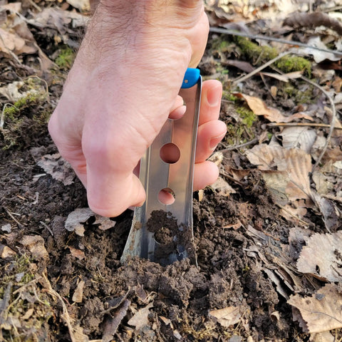 Hand using Ultralight Backpacking Trowel 0.48 Oz 13.5 G Blue With Lifetime Warranty Made In USA to dig in forest soil