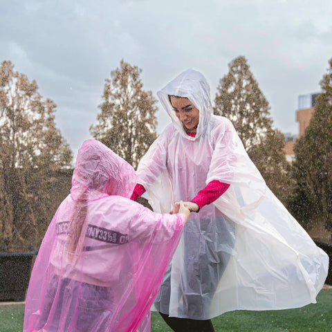 Two adults wearing Four Pack Disposable Rain Ponchos With Hood For Adults Clear See Through Emergency Rain Gear Lightweight And Waterproof.