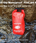 Red Well-Strong waterproof first aid kit roll-top on rocky shore, front view.