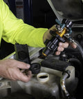 Front view of yellow and black cooling system refiller tool with hoses, held by mechanic near vehicle coolant reservoir.