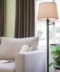 Riverside Copper Bronze Swing Arm Floor Lamp With Cozy Warm Glow Oatmeal Drum Shade in living room by a sofa and plant
