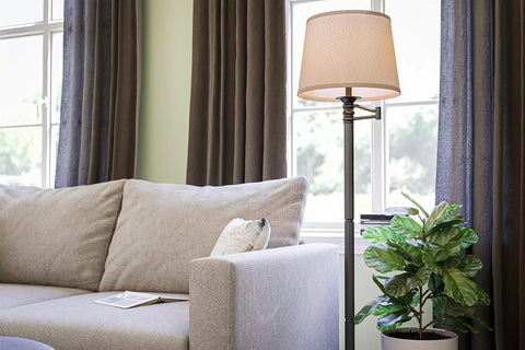 Riverside Copper Bronze Swing Arm Floor Lamp With Cozy Warm Glow Oatmeal Drum Shade in living room by a sofa and plant