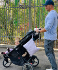 Man pushing stroller with child and Waterproof Wet Dry Bag Set for Cloth Diapers and Swimwear attached, urban park setting.