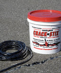 Coiled crack filler with red-lidded bucket on asphalt, labeled 125 Feet Of Blacktop Crack Filler For Asphalt And Concrete Weather Resistant No VOCs