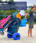 Boy pulling Heavy Duty Folding Beach Cart With Balloon Wheels Ocean Utility Carrier For The Sand, loaded with chairs and gear.