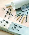 Assorted drill bits and screwdriving bits arranged on a wooden surface with metal and PVC materials.