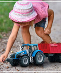 Child playing with Friction Powered Farm Tractor Trailer Toy Set 16 Inch Three Pack For Kids with blue tractor on gravel trail.