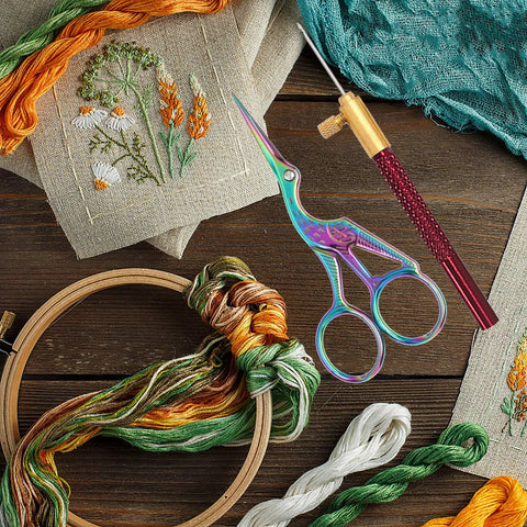 Embroidery setup with tambour hook kit, 3 needle heads, colorful threads, scissors, and embroidered cloth on a wooden surface.