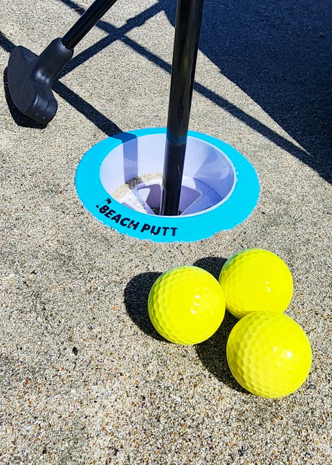 Beach Side Golf Set For The Sand With Two Adjustable Putters Waterproof Dry Bag Flags Cups Balls Sand Scoop And More For Family Fun On The Beach Game On This Summer showing yellow balls and a cup on sand.