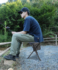 Person fishing using Two Pack Folding Camping Stools For Adults Heavy Duty Lightweight Portable Tripod Chairs in blue.