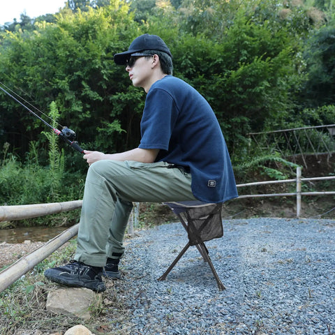 Person fishing using Two Pack Folding Camping Stools For Adults Heavy Duty Lightweight Portable Tripod Chairs in blue.