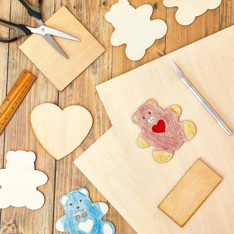 Basswood craft sheets 12x18x1/8in with assorted wooden cutouts (heart, bear, cloud) and tools on a worktable.