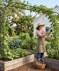 Gardener in hat tending plants under extra large garden arch trellis heavy duty galvanized metal driveway archway in yard