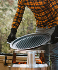 Person placing Large Cast Iron Grill Top For Bonfire And Yukon Fire Pit Outdoor Cooking Surface Seventeen And Three Quarters Inch 17 Lbs Fire Pit Accessory For Flame To Table Meals onto fire pit